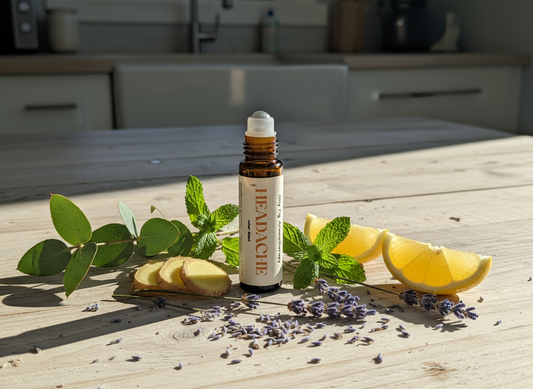 Roller bottle labeled 'Headache' on a wooden surface with lemon slices, ginger, and lavender.